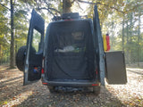 Explore nature! This **rv rental** camper van's open rear reveals a screened interior, spare tire, and gear in a sunny forest.