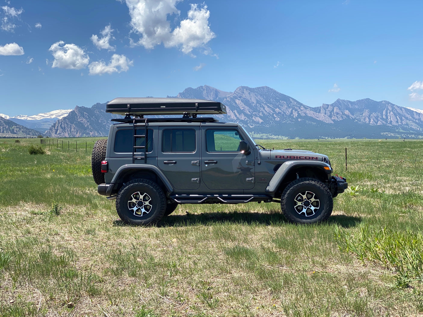 Explore nature: Gray Jeep Wrangler Rubicon with rooftop tent in a scenic mountain field, available for rv rental.