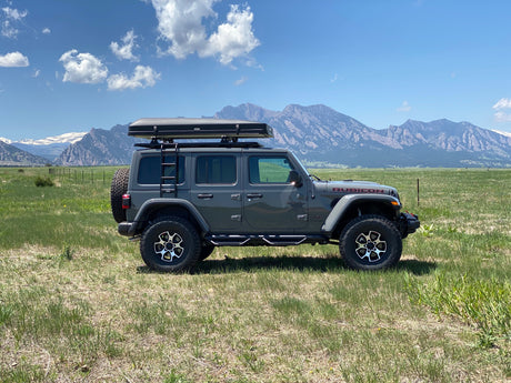 Explore nature: Gray Jeep Wrangler Rubicon with rooftop tent in a scenic mountain field, available for rv rental.