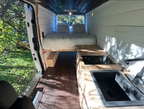 Experience van life! This rv rental showcases a beautifully converted interior with bed, kitchen, and warm lighting.
