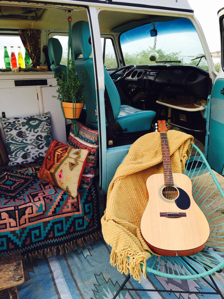 Inside a charming RV rental: cozy, boho interior with teal seats, patterned pillows, a guitar, and ocean views.