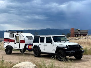 This white Jeep Wrangler tows a compact RV rental trailer, perfect for off-road camping trips in Colorado's mountains.