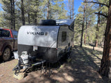 RV rental adventure: Silver Viking travel trailer & truck parked in a sunny forest with fishing rods.