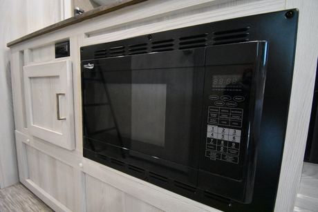 Built-in black microwave and light wood cabinetry in an RV rental kitchen, showing an electrical outlet and cabinet door.