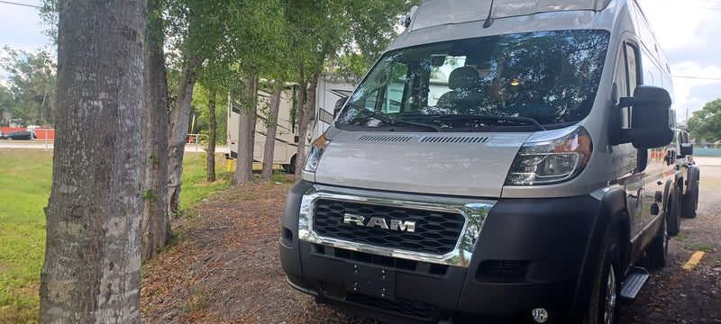  and light wood finishes. Open rear doors.|RV rental storage with a secured portable power station (green light visible) and a white charging device connected by a cable.|RV rental interior: digital dashboard (15.8 mpg) — photo 12