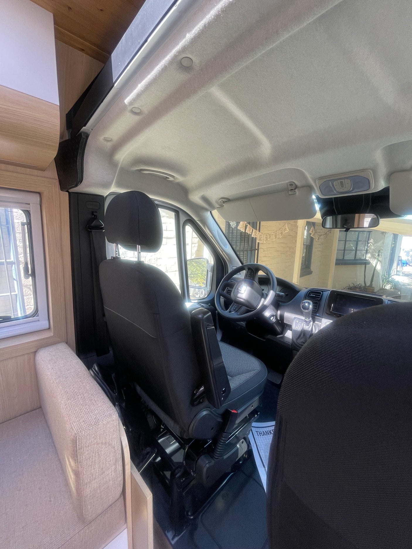 Inside a spacious RV rental camper van, showing the driver's cockpit and part of the light wood living area.