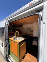 Open the door to this inviting rv rental camper van. View of a modern kitchen with sink, golden faucet, wooden ceiling, and bed.