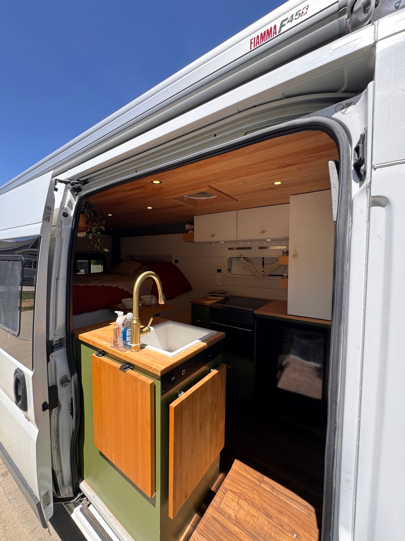 Open the door to this inviting rv rental camper van. View of a modern kitchen with sink, golden faucet, wooden ceiling, and bed.