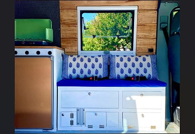 Cozy RV rental interior featuring a compact camper kitchen, comfortable blue seating with storage, and a scenic window. Perfect for van life.