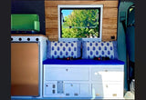 Cozy RV rental interior featuring a compact camper kitchen, comfortable blue seating with storage, and a scenic window. Perfect for van life.