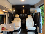 Modern RV rental interior with comfy cream seats, TV, and laptop workstation. Perfect for travel adventures.