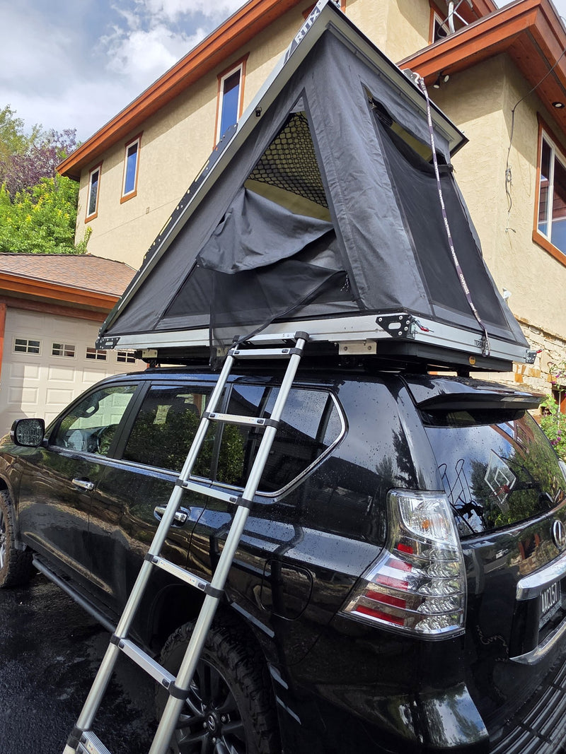 Terrapod RTTx XL opened with the telescoping aluminium ladder extended down to the ground at the rear of the vehicle, showing the rainfly and the RTTx branding on the shell end cap — photo 9