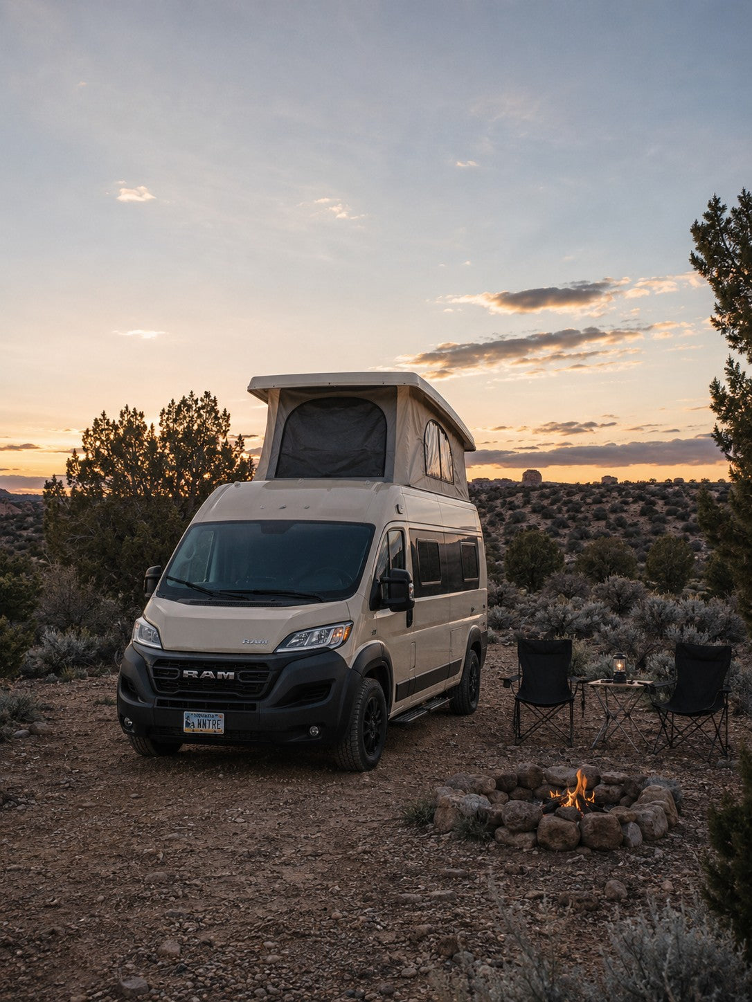 Enjoy a desert sunset from your cozy RV rental, featuring a tan camper van, campfire, and seating for two.