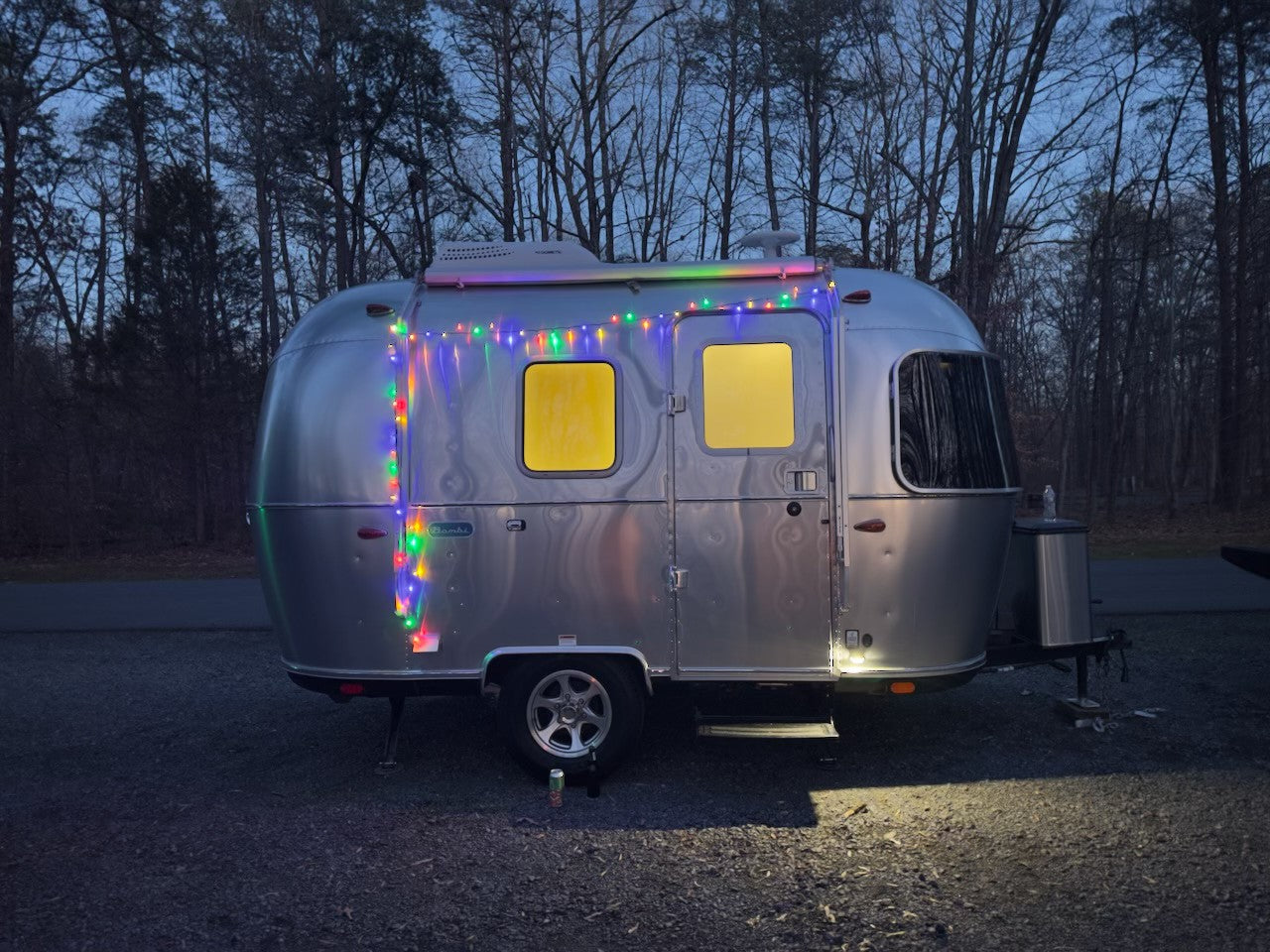 Experience a unique RV rental: this silver Airstream glows with colorful lights at night, parked in a serene forest setting.