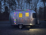 Experience a unique RV rental: this silver Airstream glows with colorful lights at night, parked in a serene forest setting.