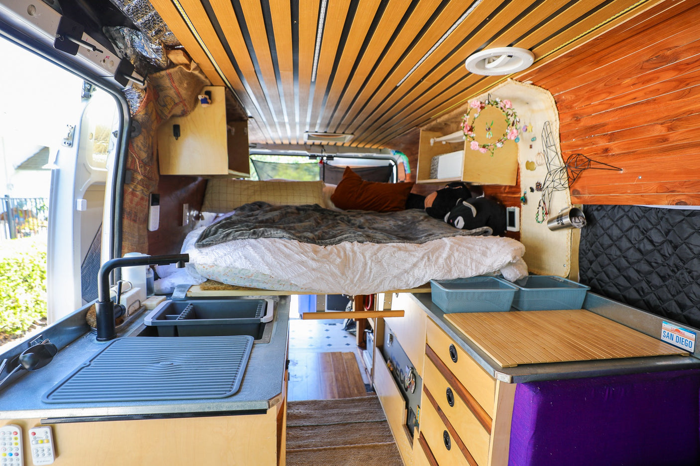 RV rental: Inside a custom camper van with a compact kitchen, elevated bed, and warm wooden interior.
