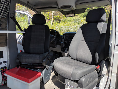 Front cabin of a spacious RV rental, with driver & passenger seats, dashboard, and built-in storage/electrical setup.