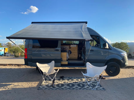 Enjoy the outdoors! This gray rv rental camper van offers an extended awning, chairs, and rug for relaxation.