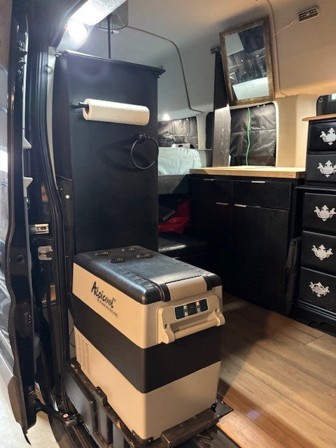 RV rental interior: an Alpicool portable fridge, paper towel holder, dark cabinets, and wood flooring visible.