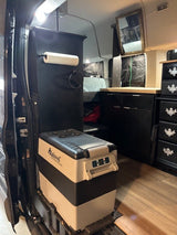 RV rental interior: an Alpicool portable fridge, paper towel holder, dark cabinets, and wood flooring visible.