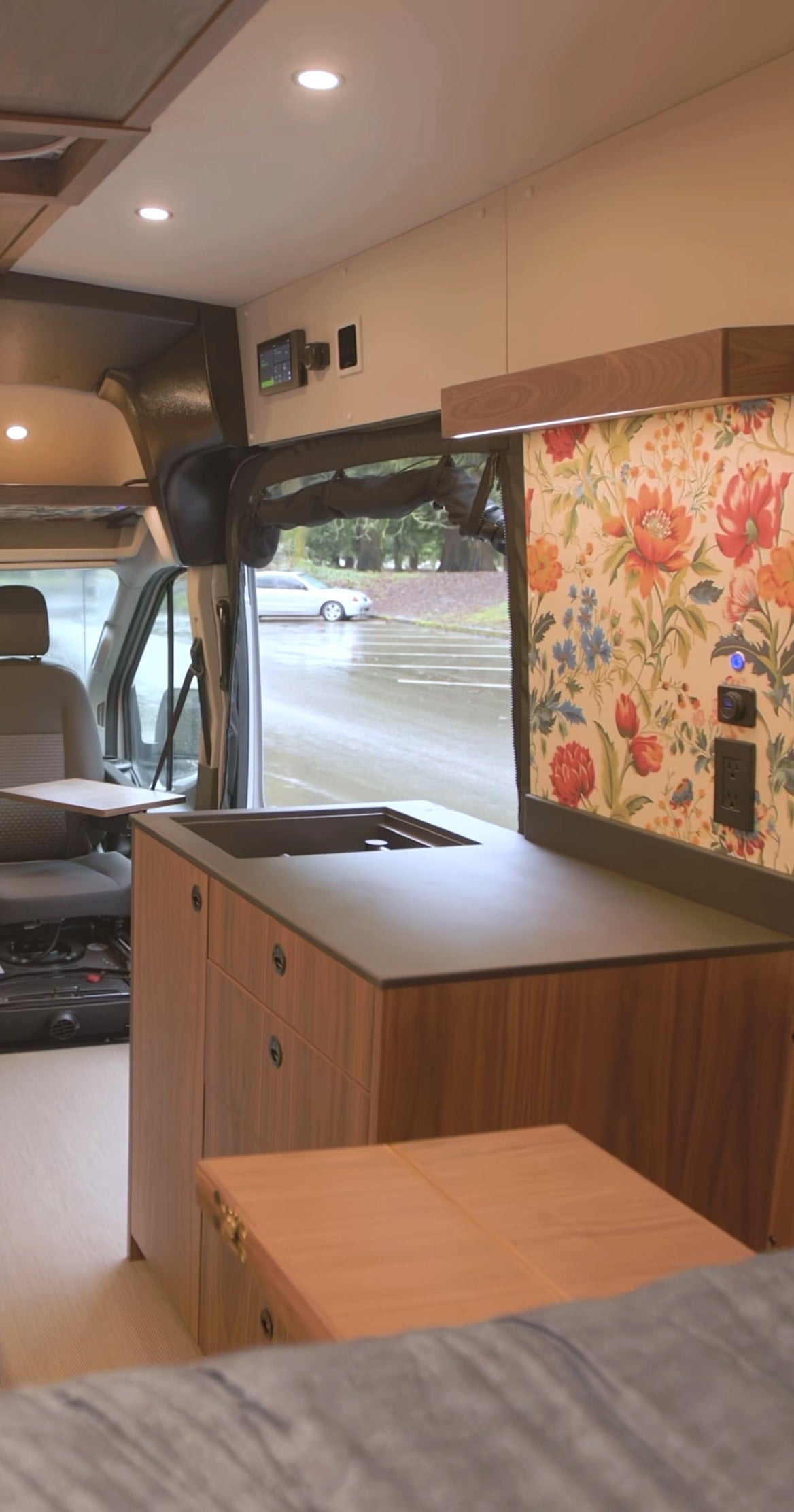 RV rental: Modern camper van interior with a compact kitchen sink, wood cabinets, and a vibrant floral accent wall, creating a cozy space.