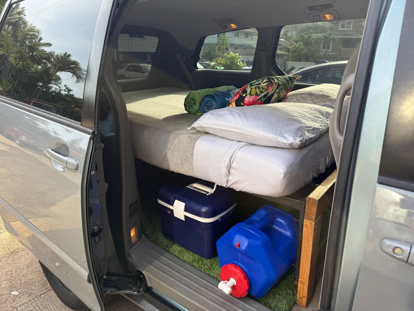 Minivan converted for van life, featuring a comfy bed, cooler, and water jug, perfect for an rv rental.
