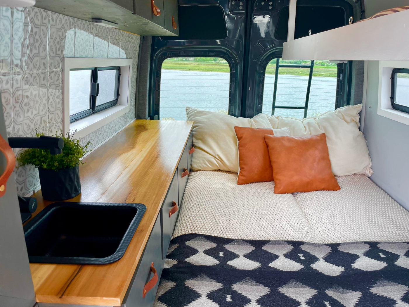Cozy rv rental interior: bed, kitchen with wood counter & sink, tiled wall, and back windows overlooking a lake. — photo 13
