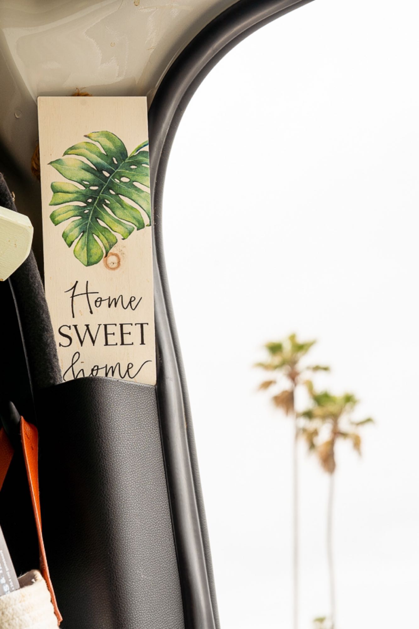 Home sweet home in your RV rental! A decorative sign with a Monstera leaf is seen inside, with palm trees in the blurry background.
