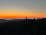 Golden sunset paints the sky above dark mountain silhouettes and distant fog. Explore these views with an RV rental!