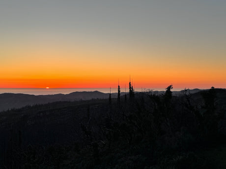 Golden sunset paints the sky above dark mountain silhouettes and distant fog. Explore these views with an RV rental!