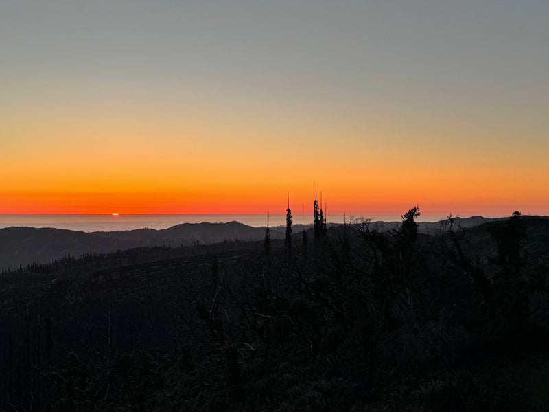 Golden sunset paints the sky above dark mountain silhouettes and distant fog. Explore these views with an RV rental! — photo 5