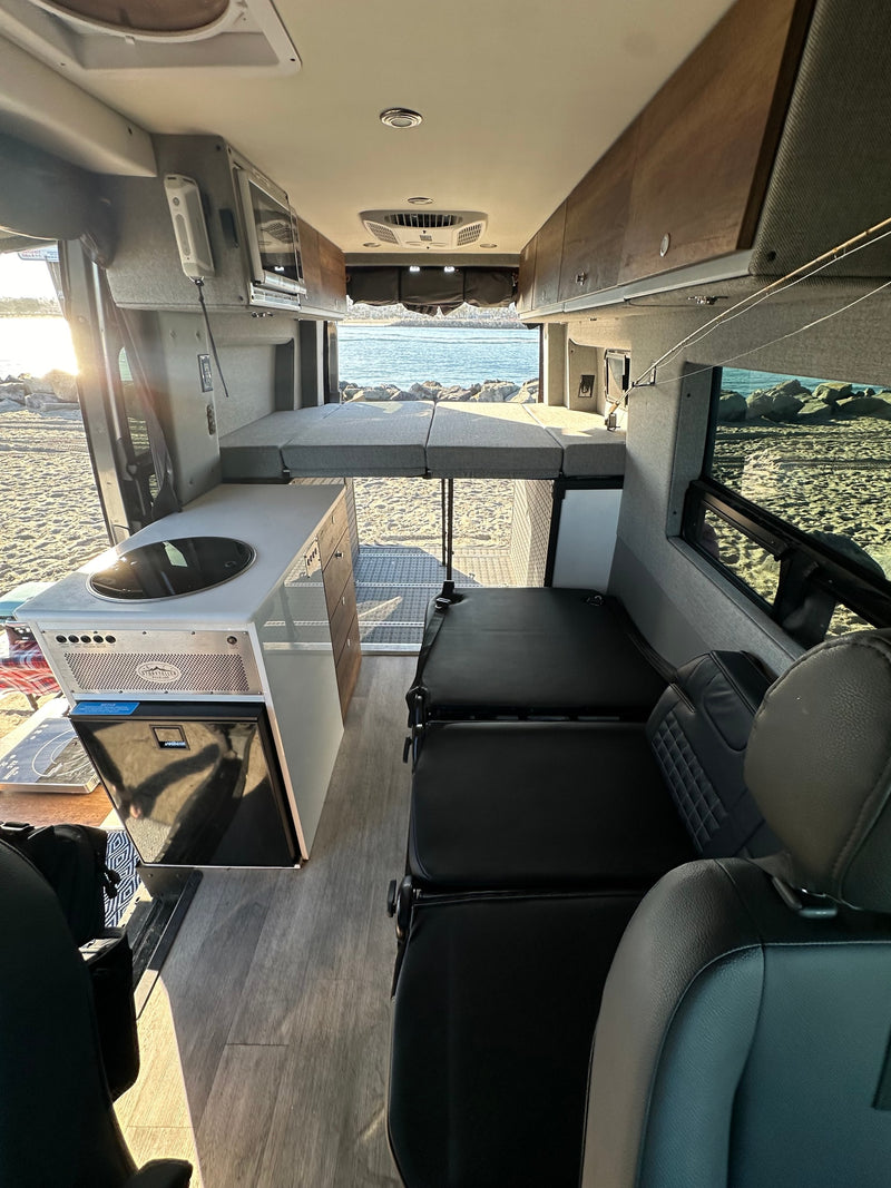 Coastal RV rental: spacious camper van interior with elevated bed, kitchenette, and beach/ocean view. — photo 8