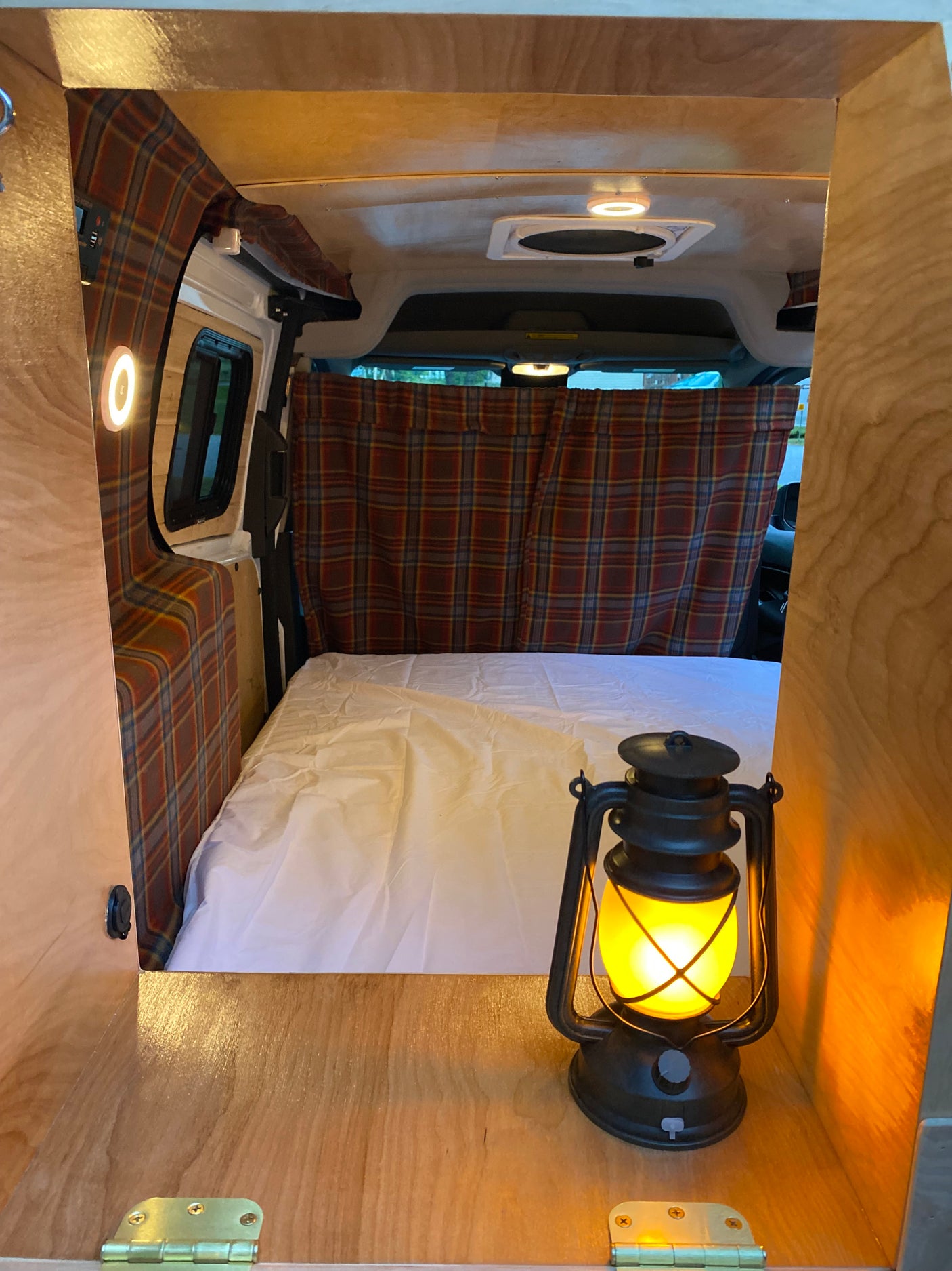 Inside a comfy **RV rental**: a bed, plaid decor, and a glowing lantern create a warm, inviting space.