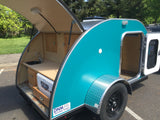 Explore this turquoise teardrop trailer, perfect for RV rental, showcasing its open rear kitchenette & side sleeping area access.