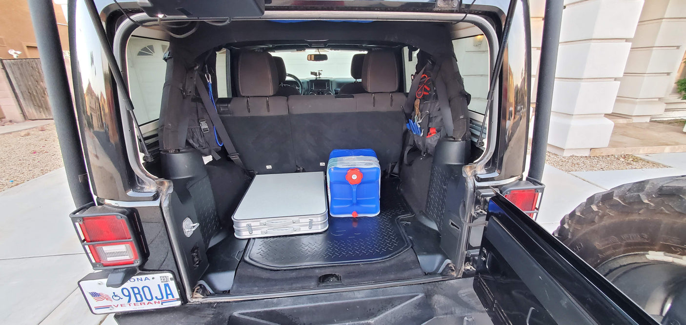 Rear cargo view of a black Jeep Wrangler, featuring a folded table & blue water jug. Prepped for outdoor adventure, an alternative to rv rental.