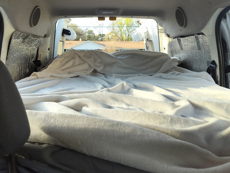 Cozy RV rental interior with a comfy bed and reflective window covers, perfect for van life adventures.