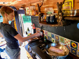Person cooks fish in an RV rental kitchen, showing a cozy van life setup with custom details and meal prep.