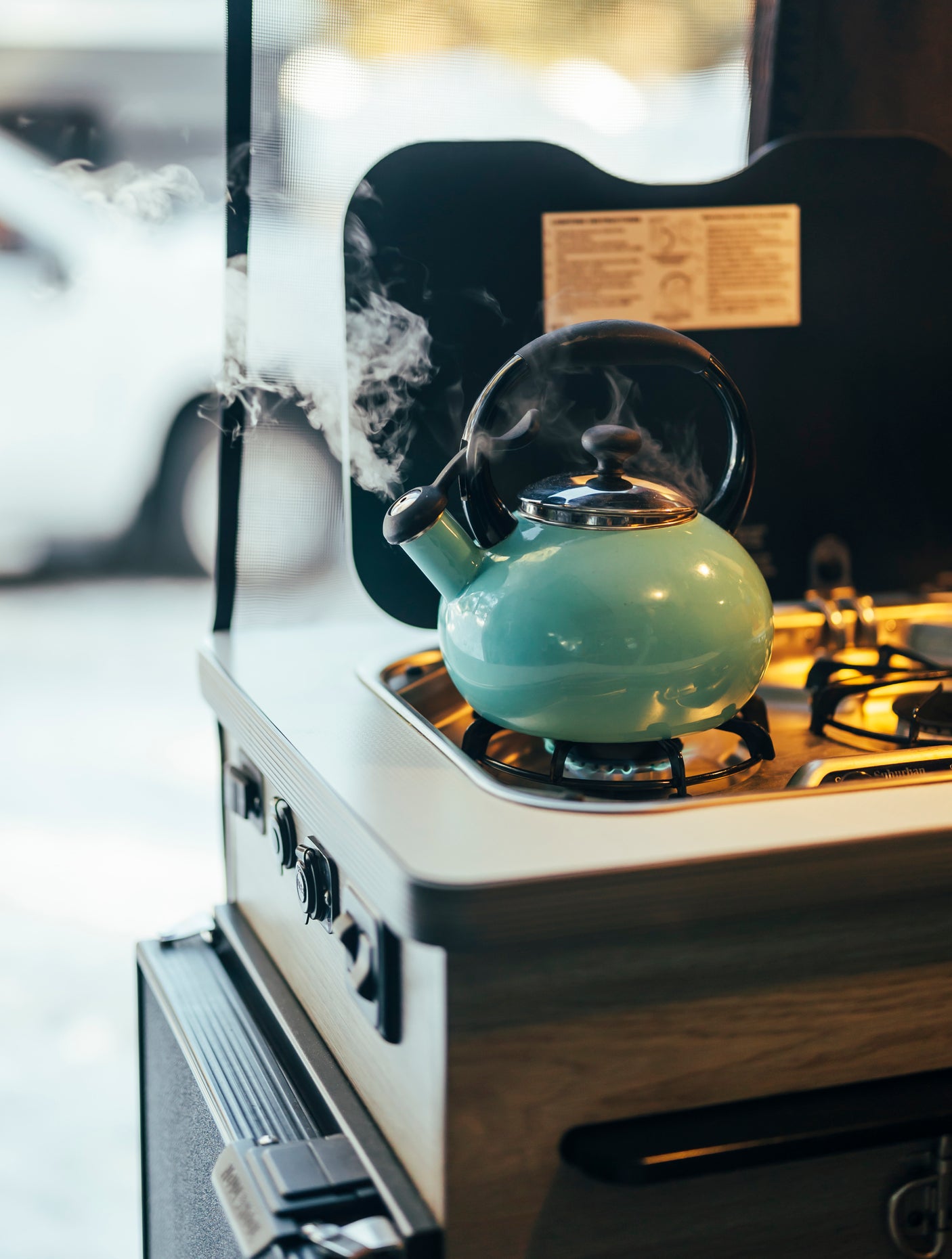 RV rental: Close-up of a teal steaming kettle on a built-in gas stove in a mobile kitchen.