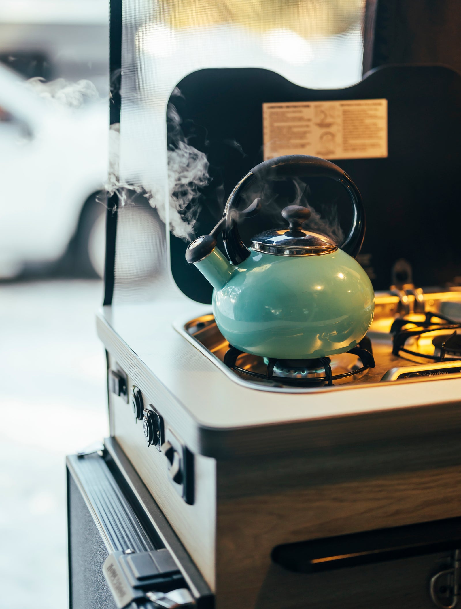 RV rental: Close-up of a teal steaming kettle on a built-in gas stove in a mobile kitchen.