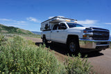 White Chevy Silverado 2500 HD truck with a Four Wheel truck camper on a dirt mountain road. Perfect for an rv rental trip.