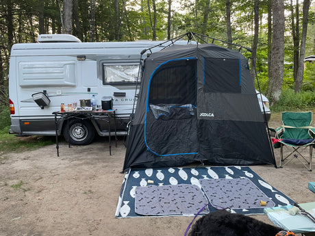 RV rental at a wooded campsite featuring an outdoor kitchen, Joolca privacy tent, and pet mats for a furry friend.