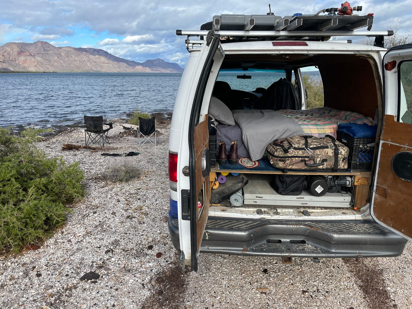 Scenic van life by the water: An RV rental with open doors shows a cozy bed and gear. Perfect for outdoor camping adventures with mountain views. — photo 5