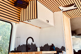 Stylish RV rental kitchen with slatted wood ceiling, unique white and black honeycomb tile backsplash, and a modern black faucet.