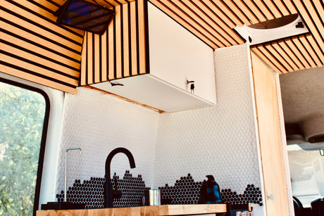 Stylish RV rental kitchen with slatted wood ceiling, unique white and black honeycomb tile backsplash, and a modern black faucet.