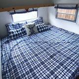 RV rental bedroom: cozy plaid bed, deer pillow, and bright windows inside a camper.
