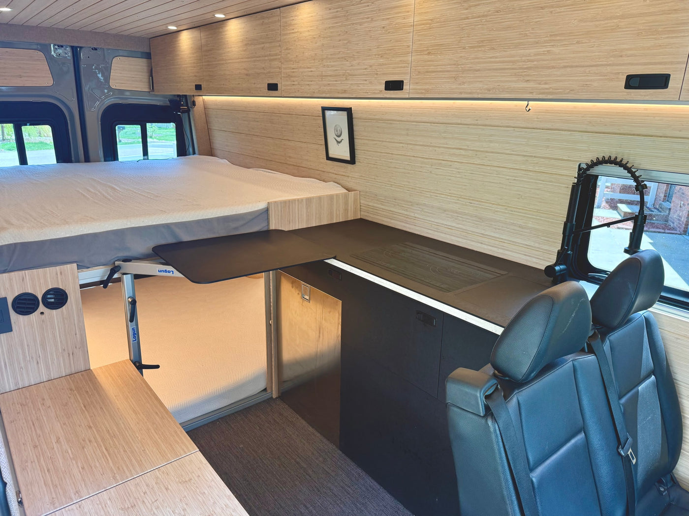 This RV rental interior showcases a raised bed, modern kitchenette with counter, flexible dining table, and passenger seating. — photo 7