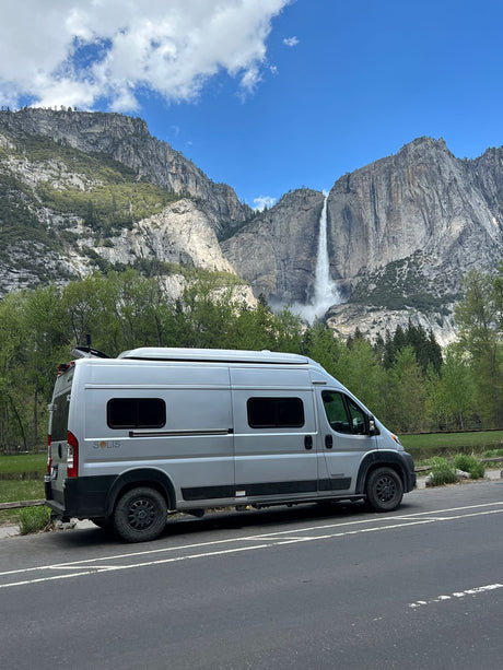A gray camper van, ideal as an RV rental, parked on a road with Yosemite Falls and grand mountains in the background.