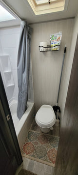 Inside an RV rental: a compact bathroom with a toilet, shower, cleaning supplies, and a small wall organizer.
