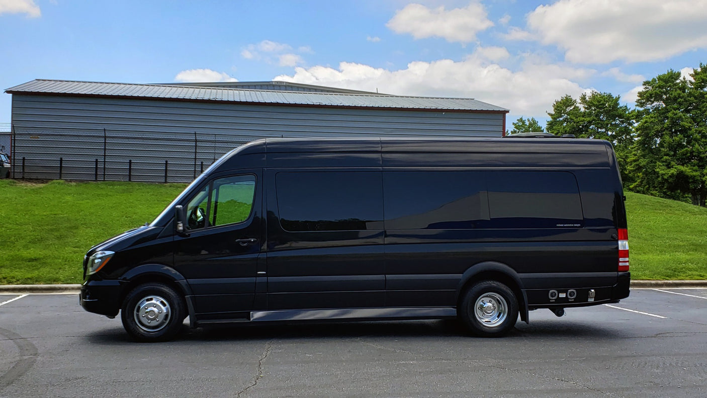 A sleek black Mercedes-Benz Sprinter luxury van, an ideal RV rental, parked on asphalt with green grass.