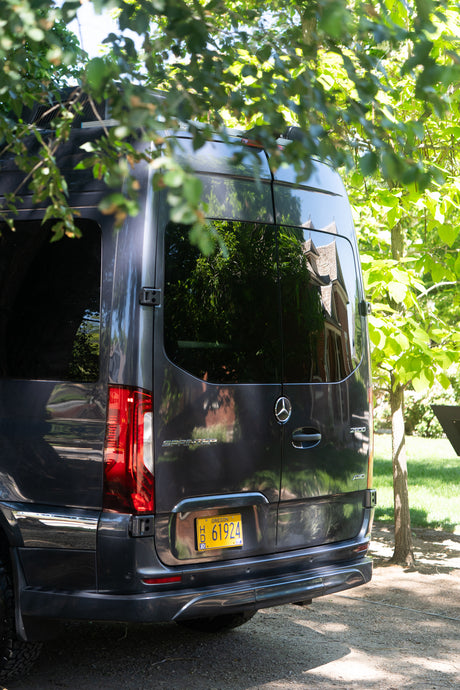 Dark grey Mercedes-Benz Sprinter van, Oregon plate H 61924, seen from rear under trees. Perfect RV rental for adventure.